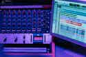 Onlineaudiomastering Blue and red audio mixer with multiple knobs and sliders, computer monitor displaying sound editing software.